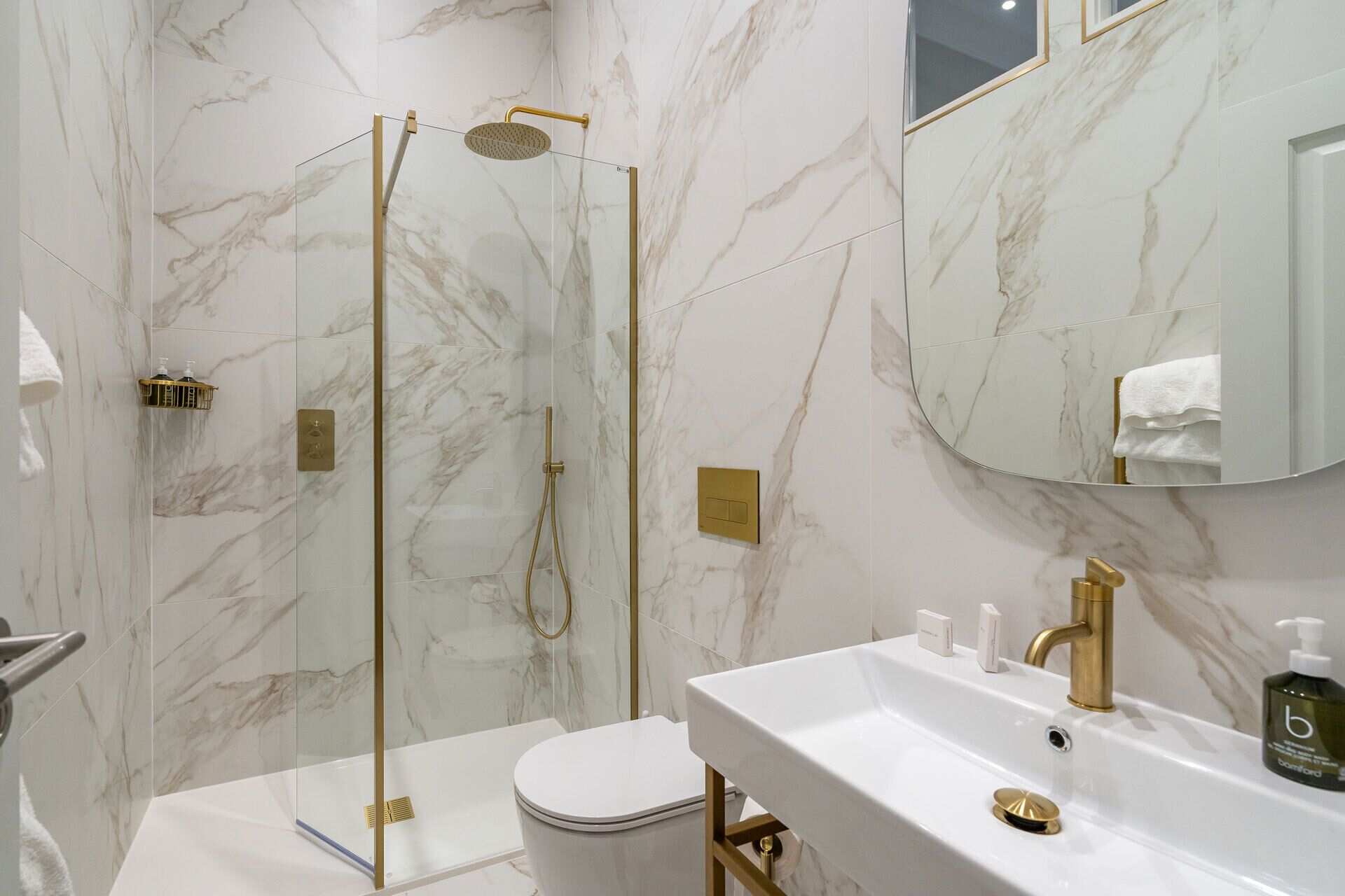 A modern bathroom with a glass-enclosed shower, a white toilet, and a sink with gold fixtures.