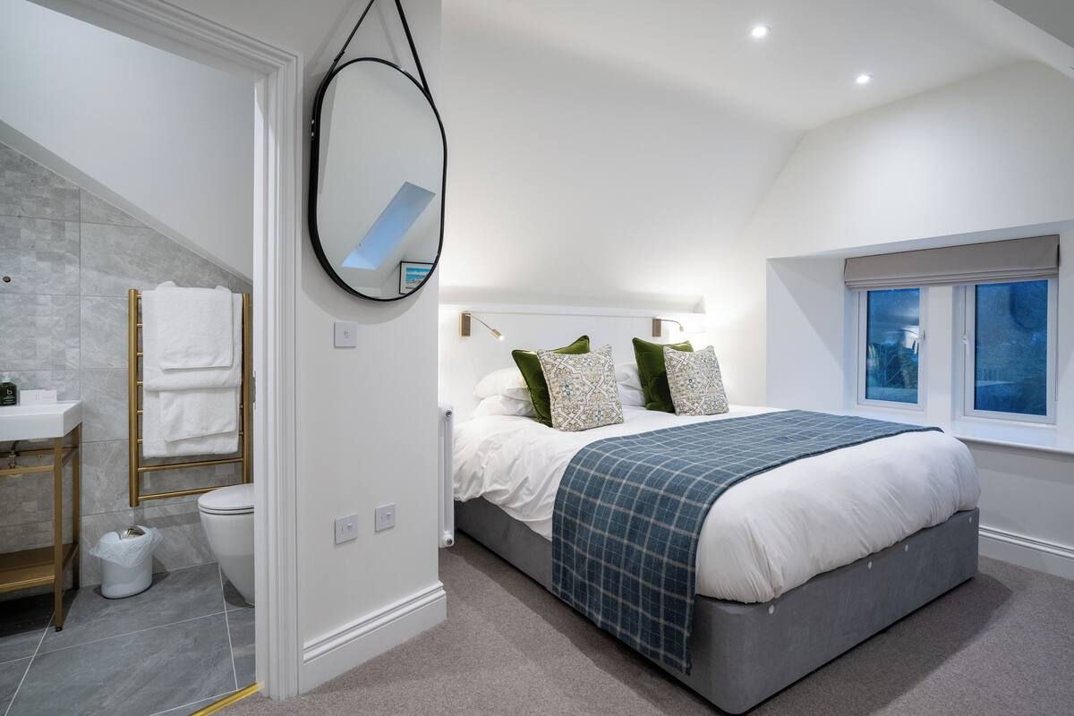 A bedroom with a bed, a window, a mirror, and a bathroom with a toilet and sink.