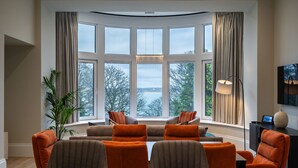 Un salon moderne avec une baie vitrée incurvée, une grande plante en pot et un téléviseur à écran plat posé sur une console sombre.