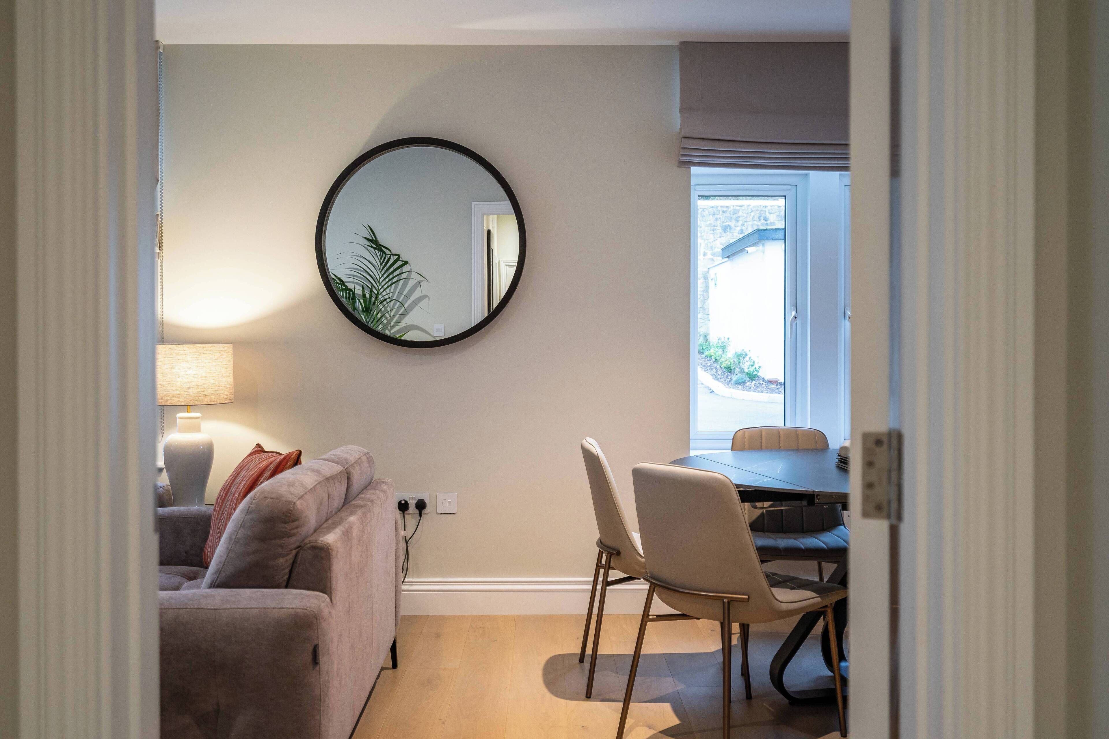 A living room with a sofa, a dining table with chairs, a lamp, and a mirror on the wall.