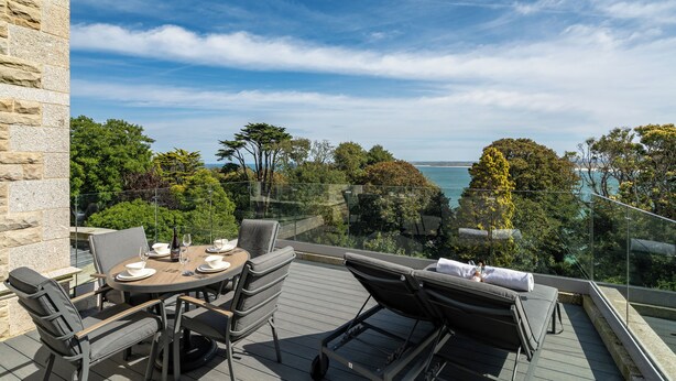 Un balcon avec une table dressée pour le dîner, des chaises longues et une vue sur la mer.