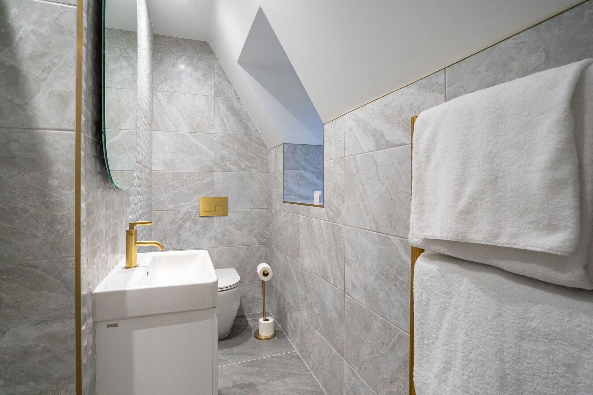 Un baño moderno con lavamanos blanco, grifería dorada, inodoro y toallero.