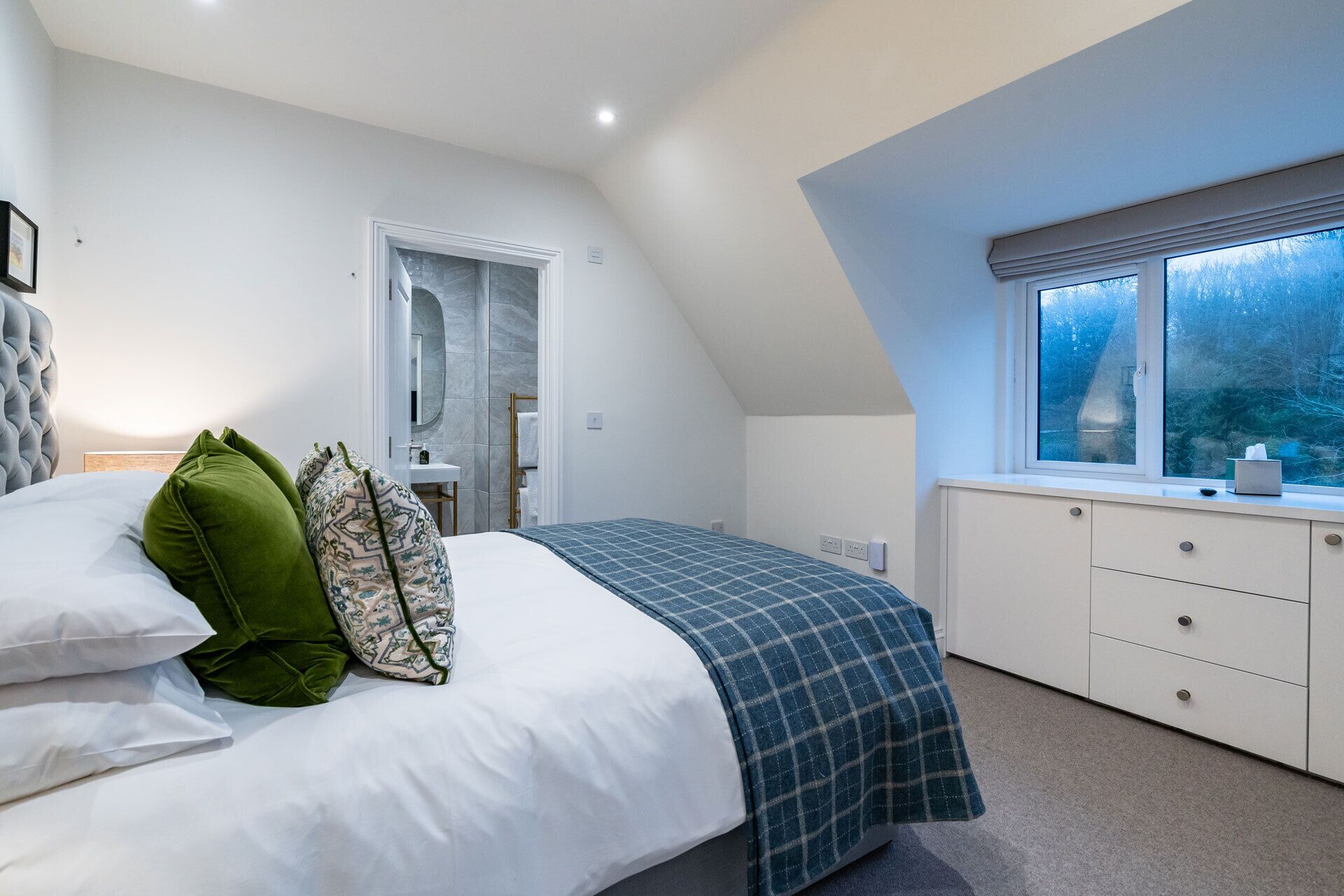 A bedroom with a bed, a dresser, a window, and a bathroom door.