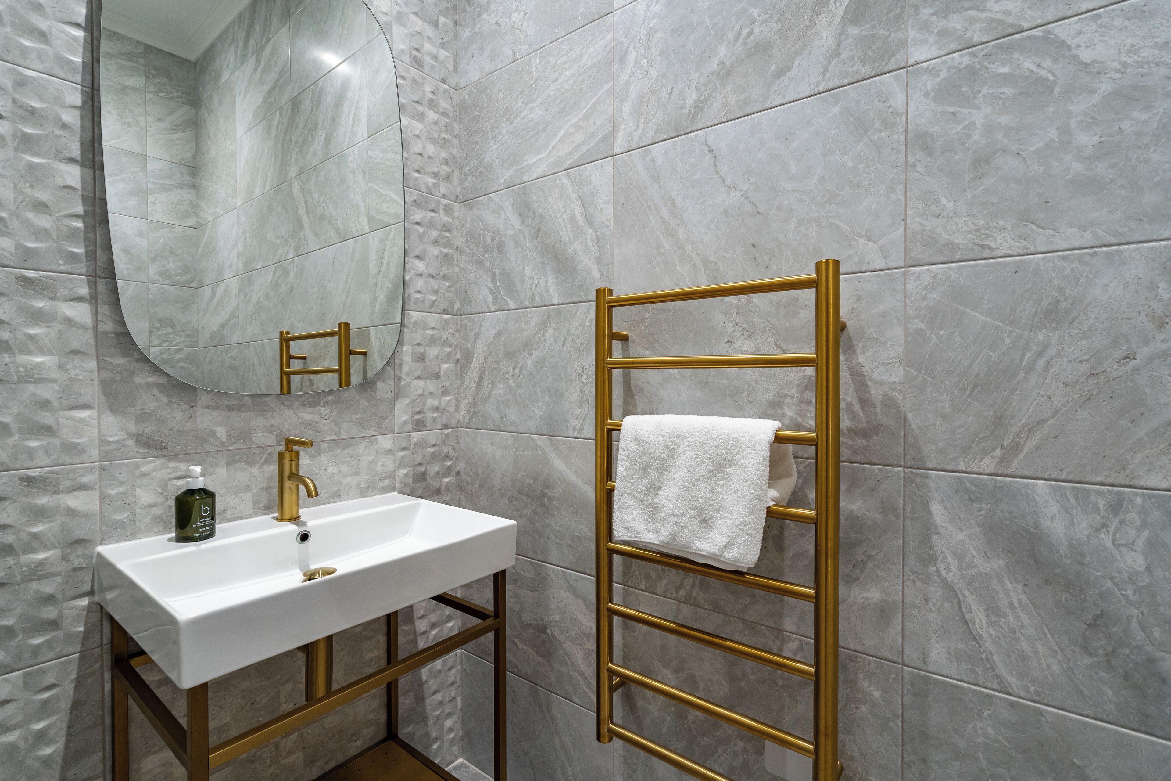 Une salle de bain avec un lavabo blanc, un robinet doré et un porte-serviettes doré sur lequel est posée une serviette blanche.