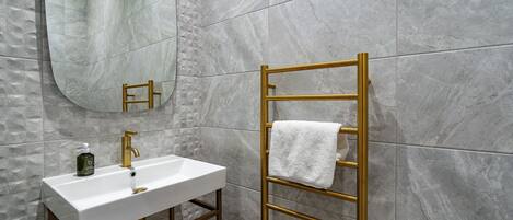 Une salle de bain avec un lavabo blanc, un robinet doré et un porte-serviettes doré sur lequel est posée une serviette blanche.