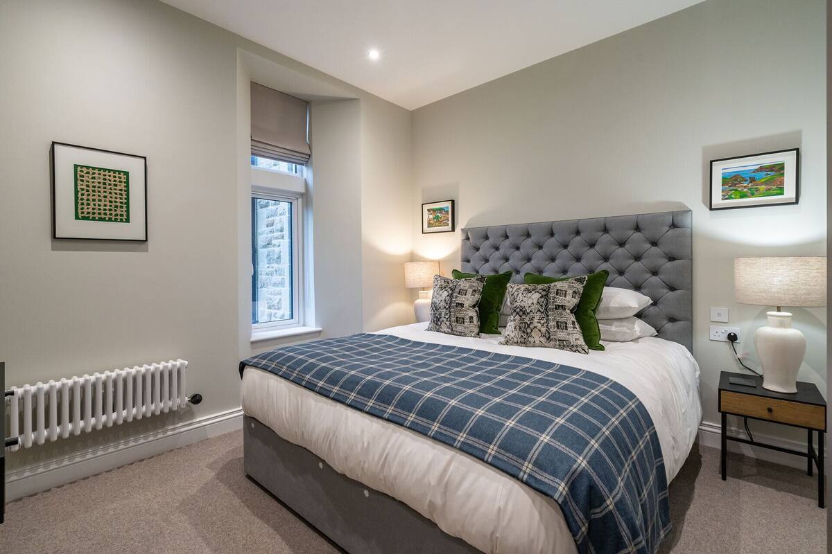 A bedroom with a large bed, a radiator, a window, and two bedside tables with lamps.