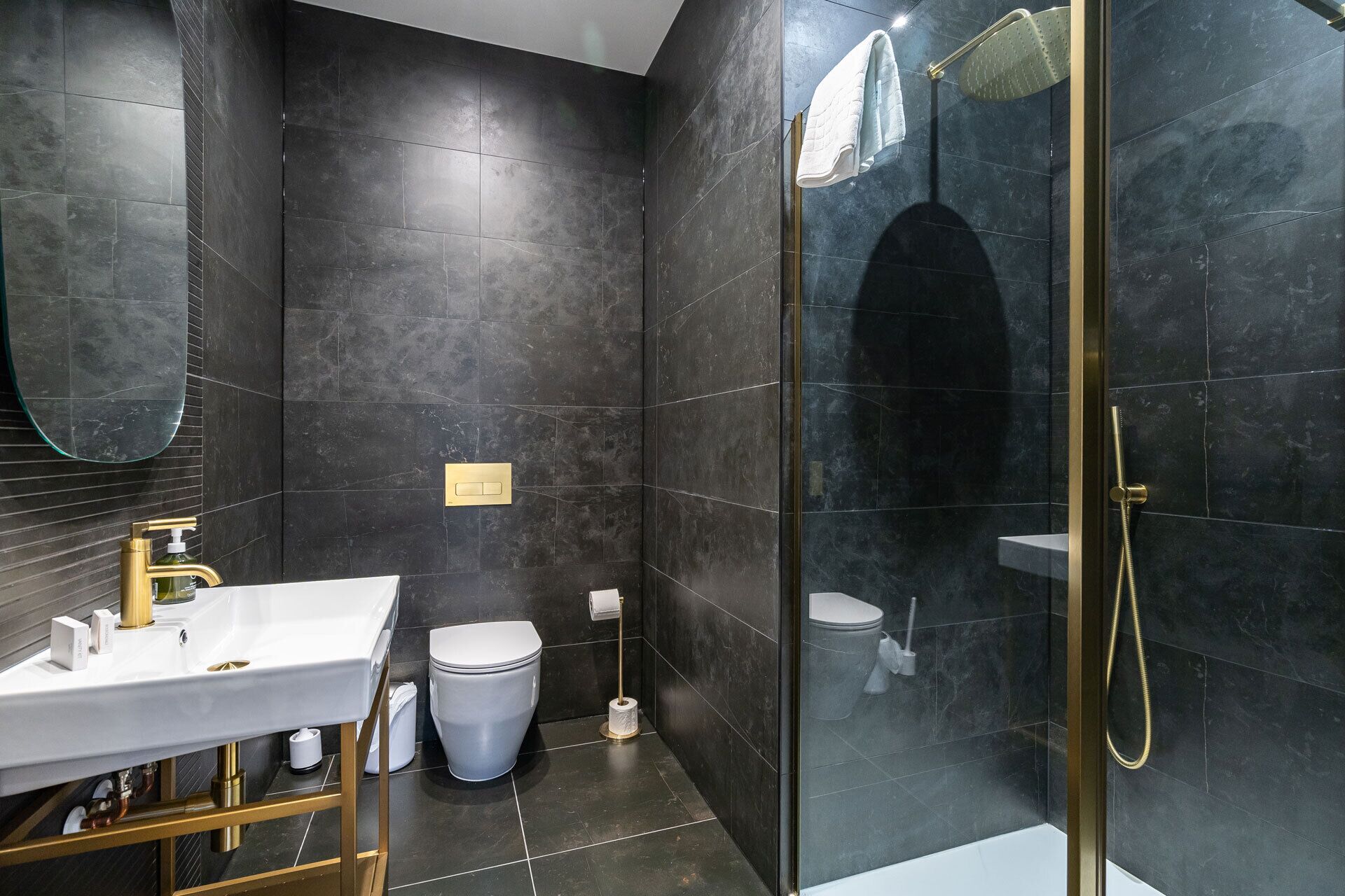 A modern bathroom with a white sink, gold fixtures, a toilet, and a glass-enclosed shower area.