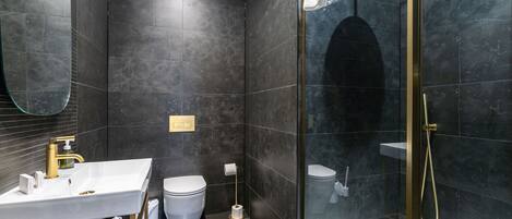 A modern bathroom with a white sink, gold fixtures, a toilet, and a glass-enclosed shower area.