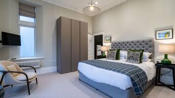 A bedroom with a large bed, a television, a wardrobe, and a window.