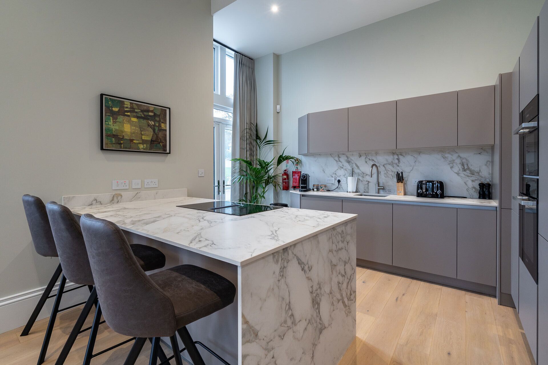A modern kitchen with a marble countertop, grey cabinets, and a dining area with bar stools.