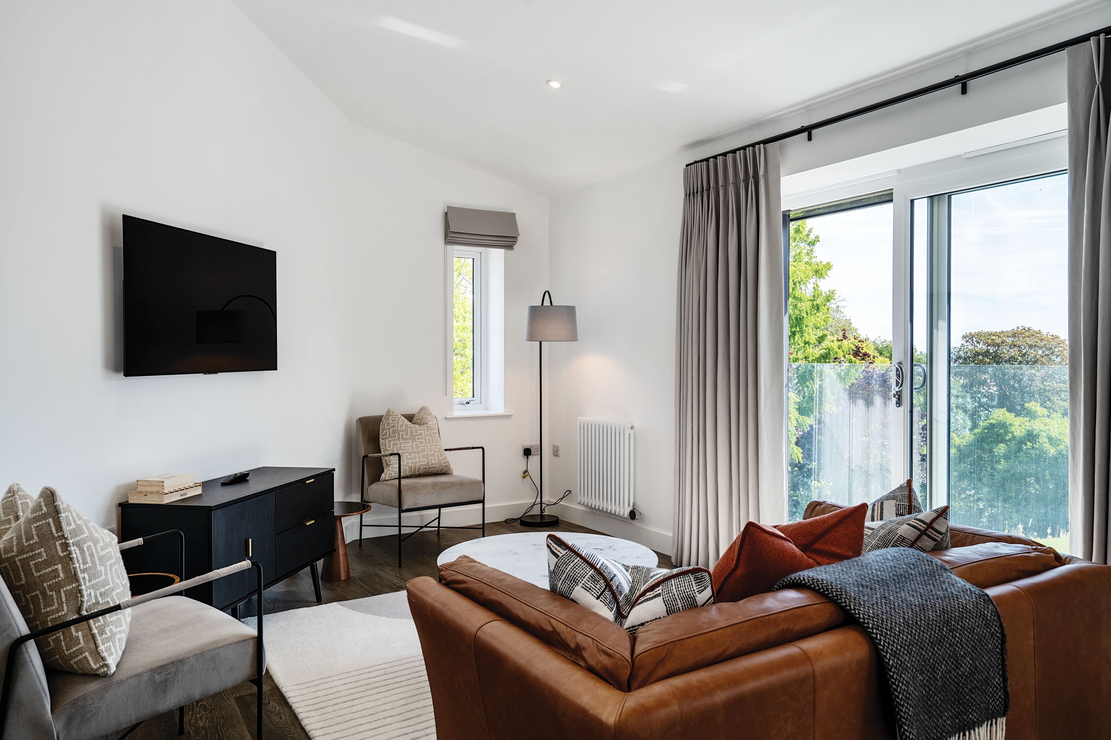 Un salon moderne avec un canapé, un fauteuil, un téléviseur et une grande fenêtre avec des rideaux.