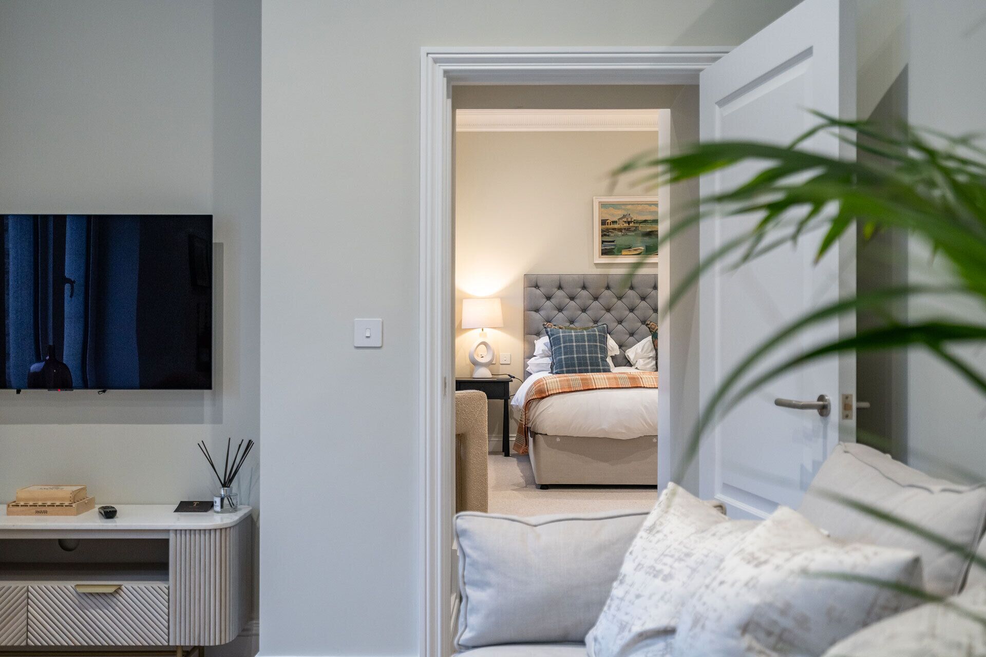 Een moderne slaapkamer met een bed, nachtkastje, lamp en een schilderij aan de muur.