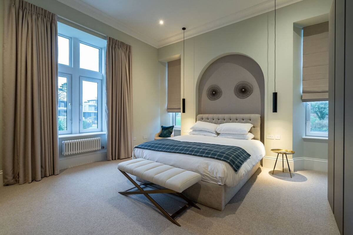 A bedroom with a large bed, a bench, a round table, and a view of the outdoors.