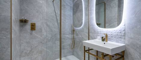 A modern bathroom with a glass-enclosed shower, a white sink with gold fixtures, and a large mirror.