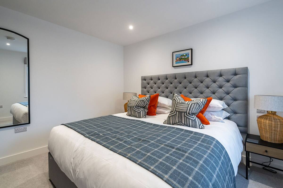 A neatly arranged bedroom with a large bed, a tufted headboard, and a bedside table with a lamp and decorative items.