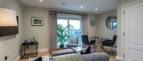 A modern living room with a sofa, a coffee table, a TV, and a dining area with chairs and a table.