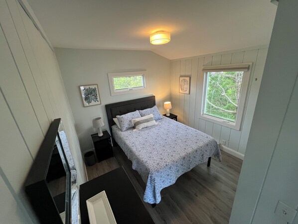 Une chambre à coucher avec un lit, des tables de chevet, une fenêtre et un luminaire au plafond.
