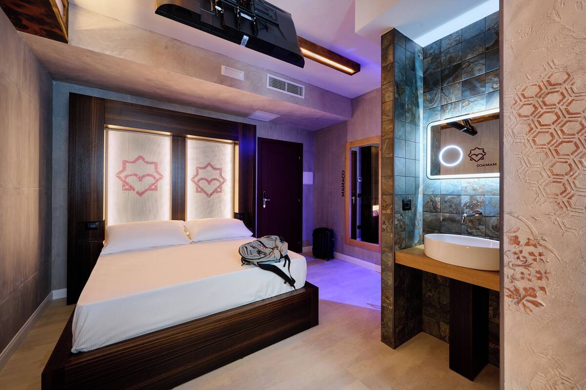 A modern hotel room with a large bed, a built-in vanity with a mirror, and a unique geometric wall design.