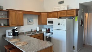 A modern kitchen with granite countertops, wooden cabinets, a built-in microwave, a refrigerator, and a coffee maker. - Charming studio in lovely Emerald Isle with beach access (Emerald Isle)