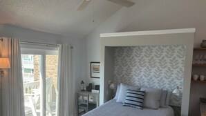 A bedroom with a bed, a desk, a chair, a ceiling fan, and a view of the outside balcony. - Charming studio in lovely Emerald Isle with beach access (Emerald Isle)