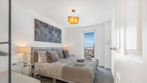 Une chambre à coucher avec un lit, des tables de chevet, une lampe, un luminaire au plafond, une fenêtre et une porte.