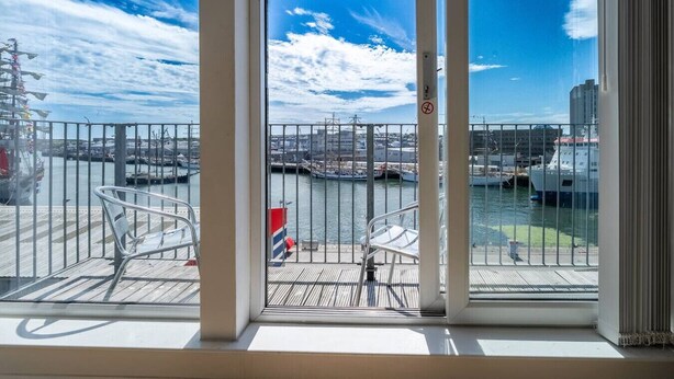 Un balcon avec des chaises en métal, une vue sur une marina avec des bateaux, et un ciel dégagé.