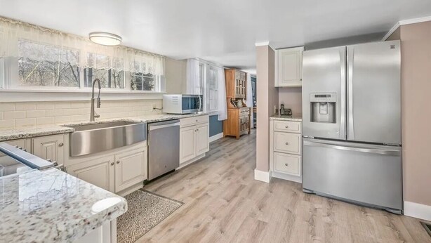 A modern kitchen with stainless steel appliances, white cabinetry, and a large window.