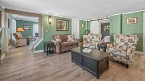 A living room with a brown sofa, patterned armchairs, a coffee table, and a staircase leading to another room.