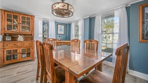Comedor con mesa y sillas de madera, aparador de madera con puertas de cristal y un ventilador de techo.