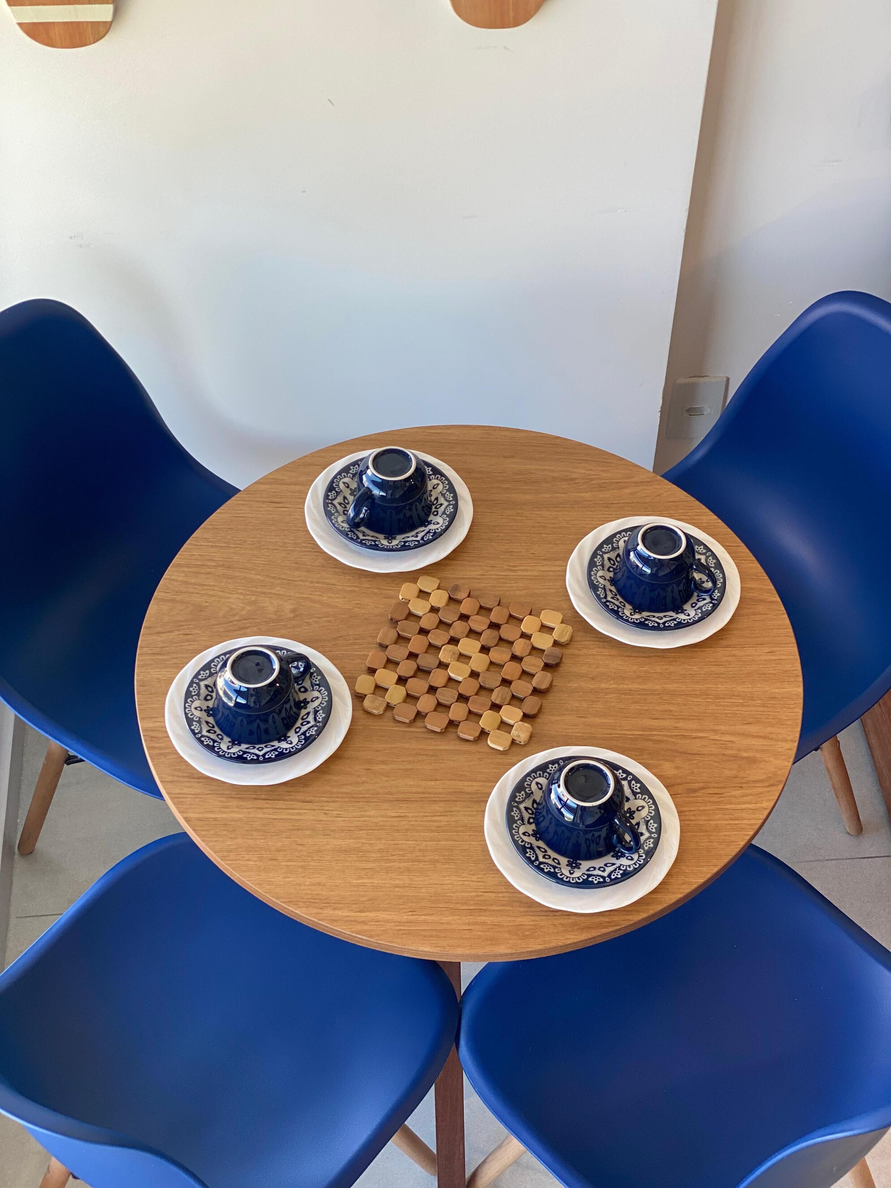 A round wooden table with four blue and white patterned cups and saucers, surrounded by four blue chairs.