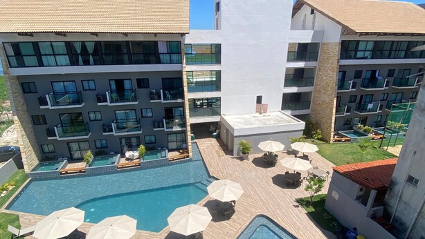 Un hotel con varias piscinas, mobiliario de exterior y vistas de los edificios circundantes.
