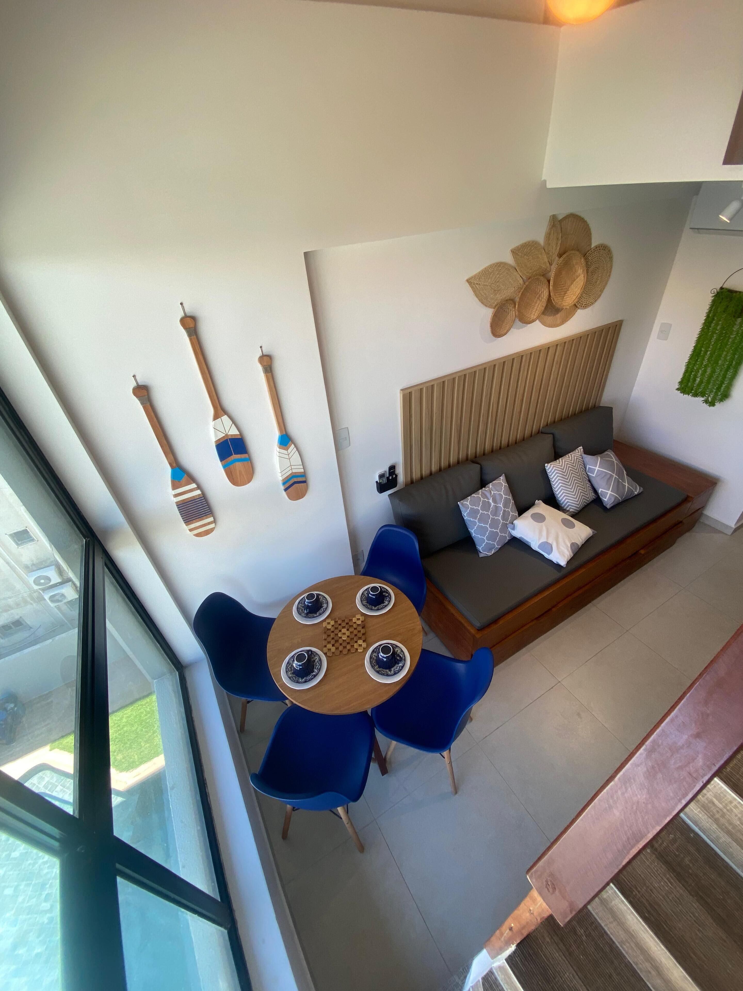 Un espacio de estar moderno con un sofá, sillas azules, una mesa de madera con cuatro tazas y objetos decorativos en la pared.