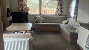 A compact living space with a sofa, a small table, a TV, and a radiator. - 3 Bed Caravan - Sleeps 6 - Pets - 5 min to Beach (Abergele)