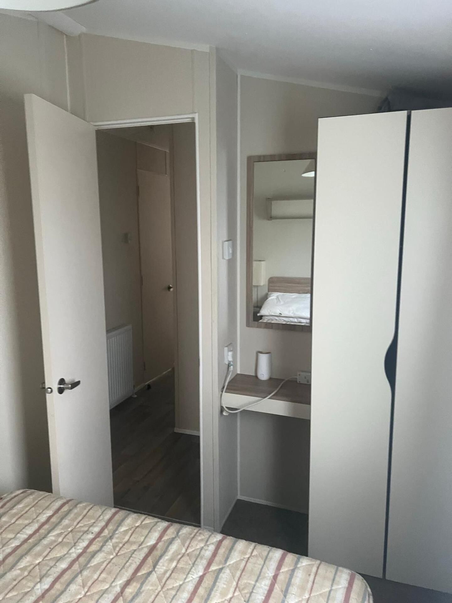 A room with a bed, a wardrobe, a mirror, and a bathroom visible through an open door.