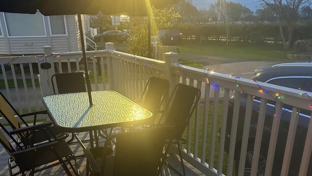 A deck with a table and chairs, a string of lights, and a car parked in the background. - 3 Bed Caravan - Sleeps 6 - Pets - 5 min to Beach (Abergele)