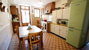 Una cocina con piso a cuadros, mesa de madera, sillas, un refrigerador verde y armarios blancos.