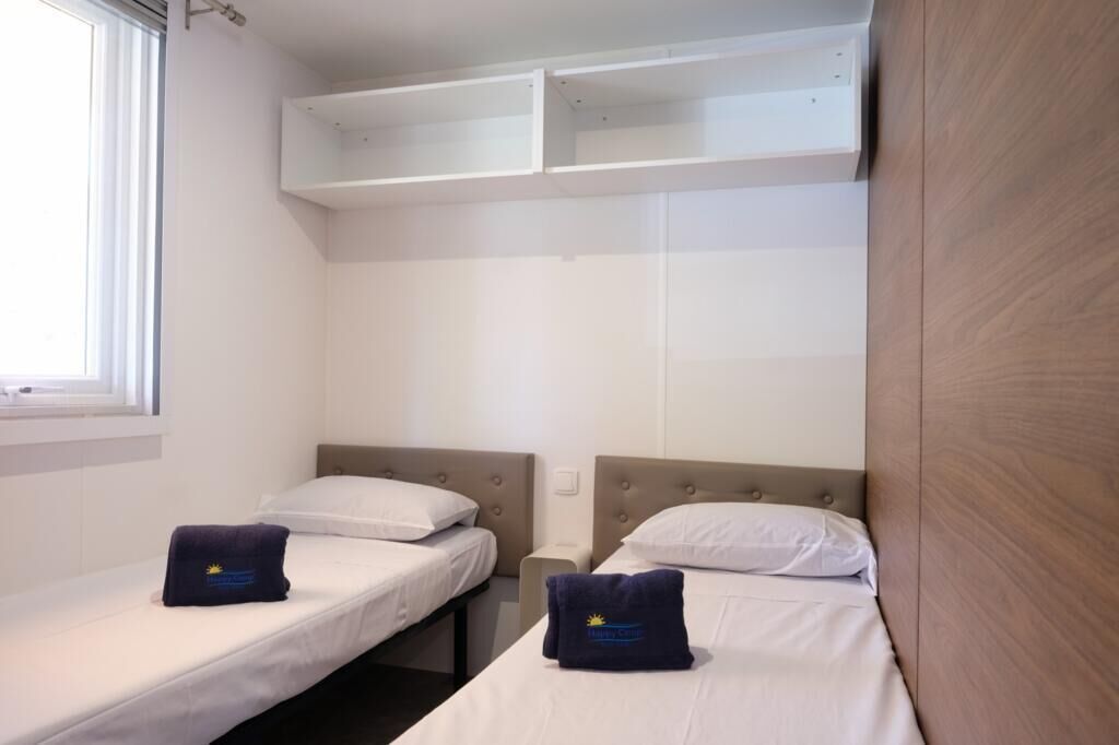 A hotel room with two single beds, a small table, and a built-in shelf above the beds.