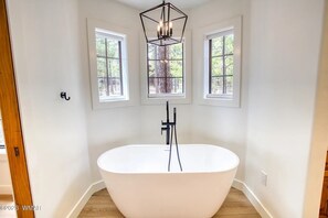 Une salle de bain moderne avec une baignoire sur pieds, trois fenêtres et un luminaire au plafond de forme géométrique.