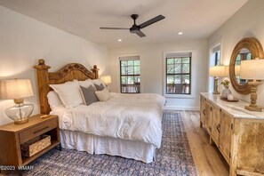 Une chambre à coucher comprenant un lit, des tables de chevet, une commode, un ventilateur de plafond et des fenêtres.