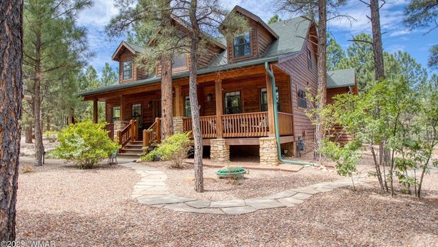 A two-story log cabin with a porch, surrounded by pine trees. - Luxurious 4-bedroom cabin with WiFi and AC in tranquil Show Low (Show Low)