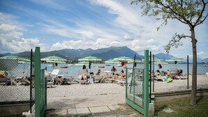 Een strand met parasols en ligbedden, een hek en bergen op de achtergrond.
