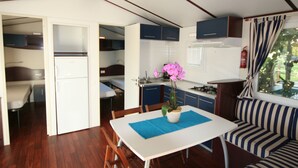 Een kleine keuken met een eethoek, een koelkast, een spoelbak en een raam met gordijnen.