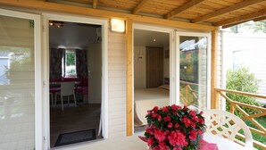 A covered outdoor seating area with a table and chairs, a flower arrangement, and a view of the backyard. - Vacation resort Baia Verde Mobile Home Suite Deluxe for 5 persons (Manerba del Garda)