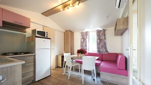 A compact kitchen with a microwave, refrigerator, and stove. There is a dining area with a table and chairs, and a pink sofa. - Vacation resort Baia Verde Mobile Home Suite Deluxe for 5 persons (Manerba del Garda)