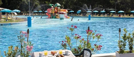A pool area with a table set for breakfast, surrounded by flowers and umbrellas.