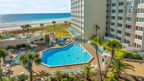 Um hotel com piscina, vista para a praia e vários andares.