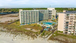Um hotel com vários andares e área de piscina, situado perto de uma praia.