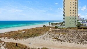 Um hotel à beira-mar com uma praia de areia, um edifício alto e um céu azul claro.