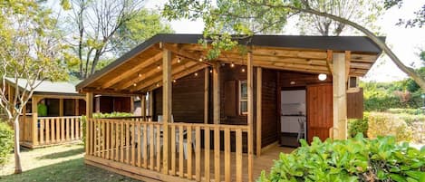 A wooden cabin with a deck, surrounded by trees and a well-maintained lawn.