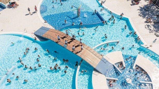Une grande piscine extérieure dotée de plusieurs couloirs et d’une zone de pont en bois.